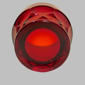 May include: A deep red glass candle holder with a faceted design. The holder has a round opening at the top.