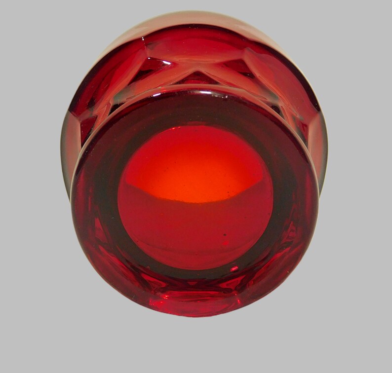 May include: A deep red glass candle holder with a faceted design. The holder has a round opening at the top.