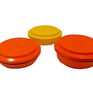 May include: Three round plastic containers with lids. Two are orange and one is yellow.