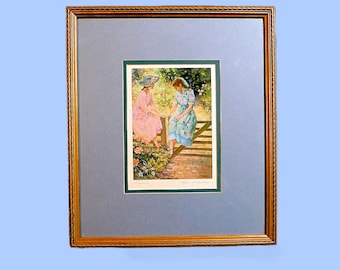 May include: A framed print of a watercolour painting showing two people in a garden. The print is set within a gold-coloured frame, with a blue-grey mount. The painting depicts two people seated on a bench, surrounded by flowers and greenery.