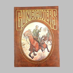 May include: A hardcover book titled "Gunfighters" with a brown leather-like cover. The cover features a gold-colored title and an oval illustration of a man on horseback, holding a gun. The illustration is in a vintage style.