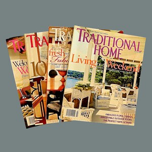 May include: A stack of four magazines with the title "TRADITIONAL HOME" on the top magazine. The magazine covers feature images of a porch, a room with a fireplace, and a room with a window. The text on the covers includes "Living for the Weekend" and "Fresh and Fab".