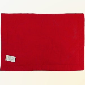 May include: A solid red rectangular throw pillow with a white label attached to the bottom left corner.