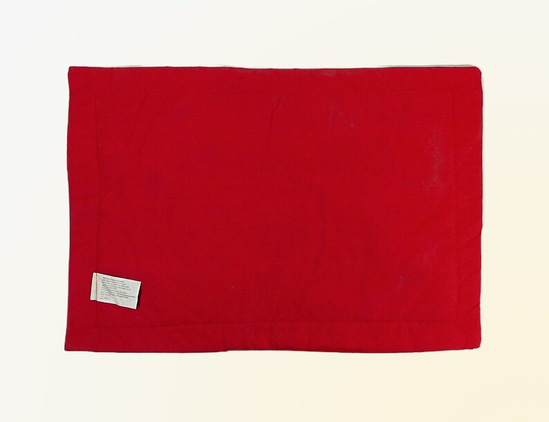 May include: A solid red rectangular throw pillow with a white label attached to the bottom left corner.