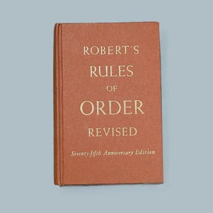 May include: A brown book titled "Robert's Rules of Order Revised" with the text "Seventy-fifth Anniversary Edition" on the bottom.