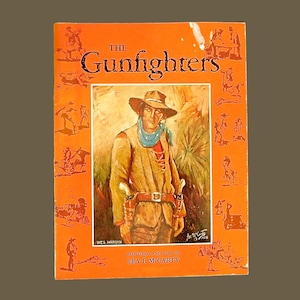 May include: A vintage book cover with an orange background and the title "The Gunfighters" in bold, white letters. The cover features a painting of a cowboy wearing a brown jacket, blue scarf, and a brown hat. The text "Paintings and Text by Lea E. McCarty" is at the bottom of the cover.