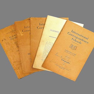 May include: A stack of five vintage brown paperbound books with the title "International Correspondence Schools" on the top book. The book is titled "Instruction Paper on Telegraphy, Part 1".