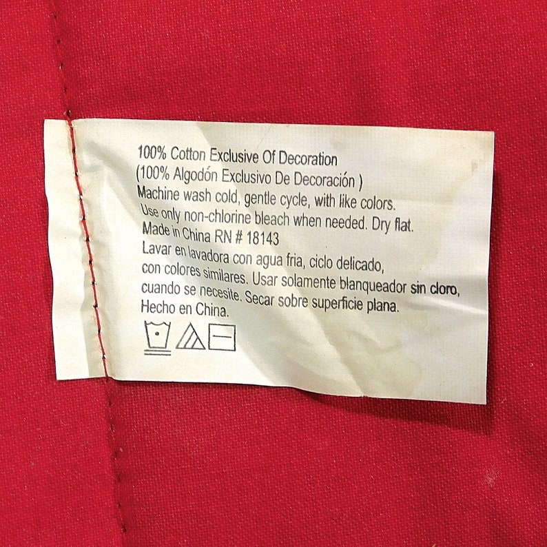 May include: White care label with black text and symbols. The text reads "100% Cotton Exclusive Of Decoration (100% Algod&oacute;n Exclusivo De Decoraci&oacute;n) Machine wash cold, gentle cycle, with like colours. Use only non-chlorine bleach when needed. Dry flat. Made in China RN #18143 Lavar en lavadora con agua fria, ciclo delicado, con colores similares. Usar solamente blanqueador sin cloro, cuando se necesite. Secar sobre superficie plana. Hecho en China."