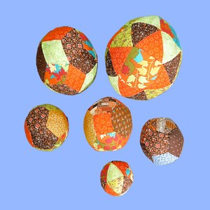 May include: Six colourful patchwork fabric balls in various sizes and patterns. The balls are made of different fabrics in shades of brown, orange, green, and blue.