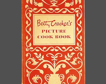 May include: A vintage cookbook titled "Betty Crocker's Picture Cook Book" with a red cover and cream-colored decorative floral and scrollwork design. The title is in a rectangular cream-colored box.