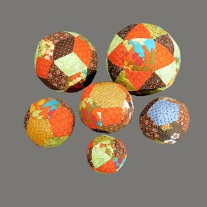 May include: Six colourful patchwork fabric balls in various sizes and patterns. The balls are made of different fabrics in shades of brown, orange, green, and blue.