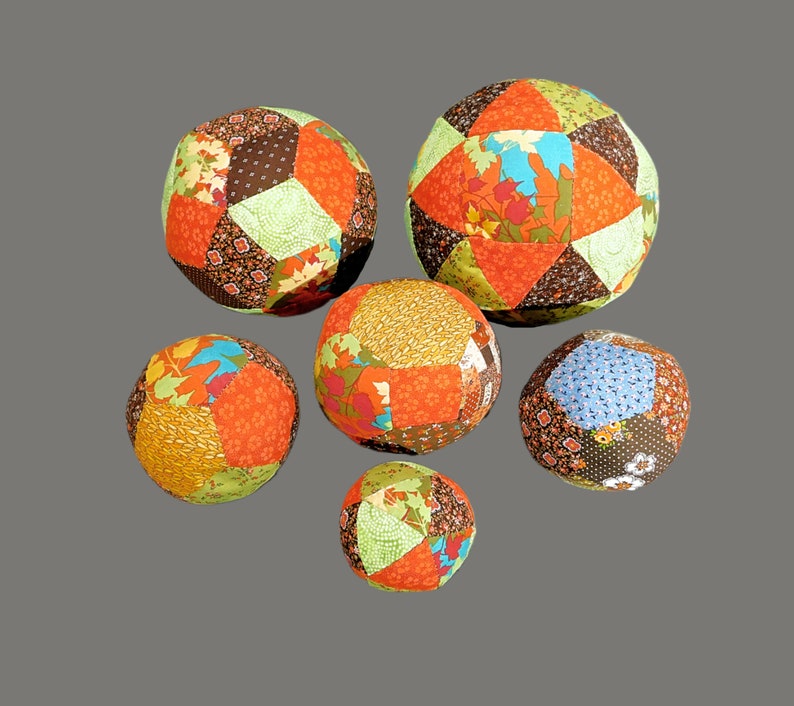 May include: Six colourful patchwork fabric balls in various sizes and patterns. The balls are made of different fabrics in shades of brown, orange, green, and blue.