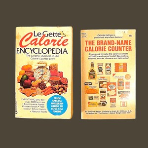 May include: Two vintage paperback books on a brown background. The first book is titled "Le Gette's Calorie Encyclopedia" with a colorful illustration of fruits and vegetables. The second book is "The Brand-Name Calorie Counter" with food product images.