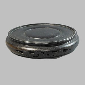 May include: A black wooden pedestal with intricate carvings around the base. The pedestal is round and has a smooth, polished surface.