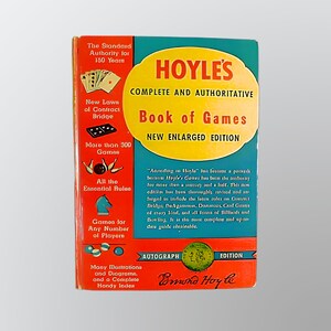 May include: A vintage copy of "Hoyle's Complete and Authoritative Book of Games." The cover is teal and red with the title in yellow. Text includes "New Enlarged Edition" and "Autograph Edition."