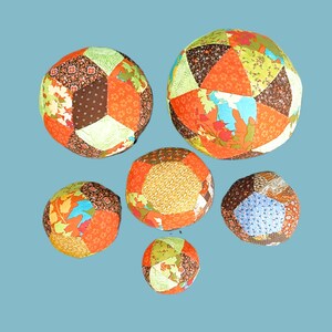 May include: Six colourful patchwork fabric balls in various shades of orange, brown, green, and blue. The balls are made of different patterned fabrics sewn together.
