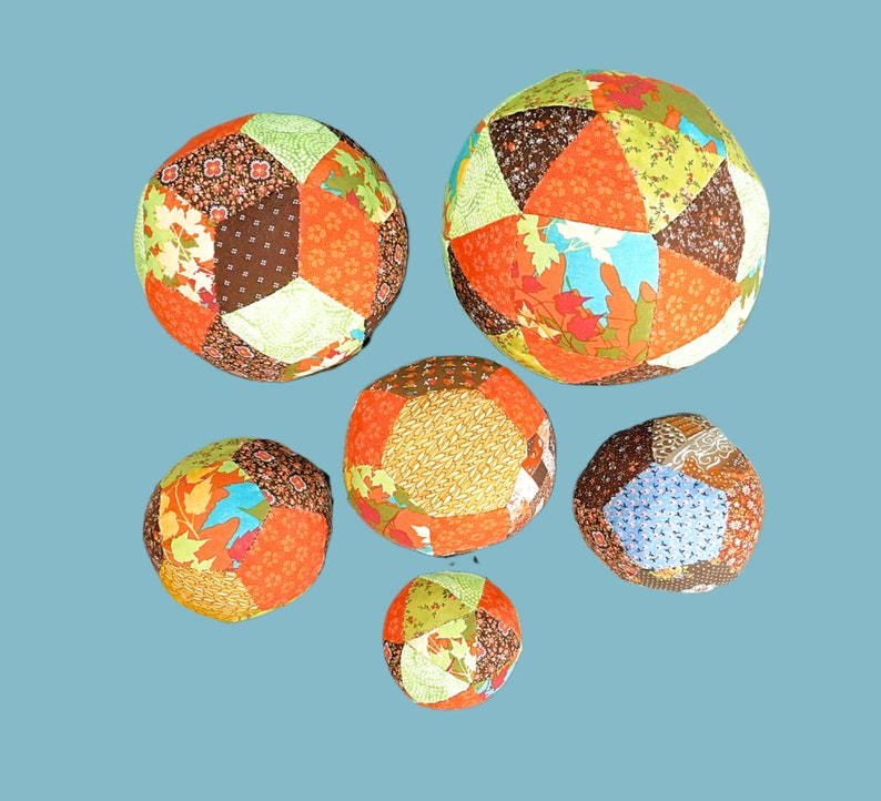 May include: Six colourful patchwork fabric balls in various shades of orange, brown, green, and blue. The balls are made of different patterned fabrics sewn together.