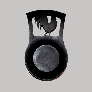 May include: A black metal spoon rest with a rooster cutout design. The spoon rest has a circular base and a handle with the rooster silhouette. The overall design is simple and functional, suitable for kitchen use.