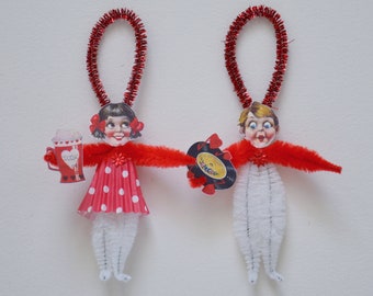 May include: Two vintage-style pipe cleaner ornaments, one with a red dress and a soda cup, the other with a white suit and a record. Both have red glitter pipe cleaner hair and red glitter pipe cleaner loops for hanging.