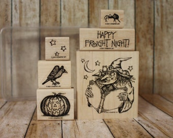 May include: A set of five wooden stamps with Halloween themes. The stamps feature a witch reading a book, a pumpkin, a raven, stars, and a spider. The stamps are all in black and white and have a vintage look.