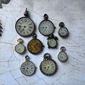 May include: A collection of ten antique-style clock charms in various sizes and finishes. The charms feature Roman numeral clock faces with black hands and are made of metal with a gold or silver finish.
