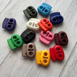 May include: Assortment of colorful plastic toggle cord locks in various colors, including green, blue, red, brown, black, white, pink, and yellow.