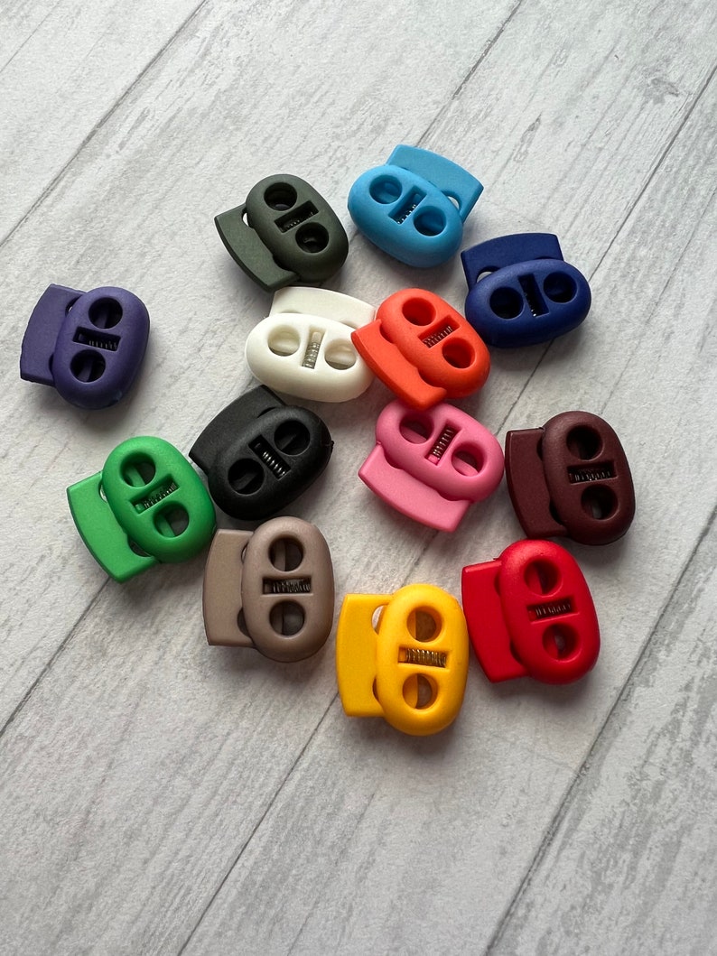 May include: Assortment of colorful plastic toggle cord locks in various colors, including green, blue, red, brown, black, white, pink, and yellow.