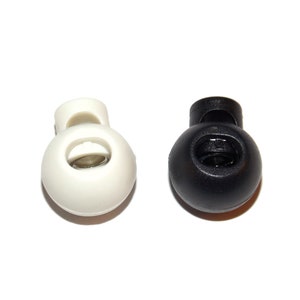 May include: Two plastic toggle stoppers, one white and one black. Both have a round shape with a hole in the center.
