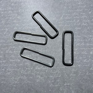 May include: Four metal key rings, two silver and two black, arranged in a starburst pattern on a gray background.