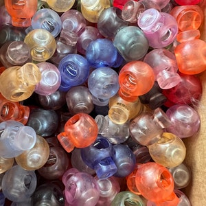 May include: A large assortment of plastic toggle clasps in various colors, including clear, blue, red, orange, green, and purple. The clasps are round and have a small metal spring inside.