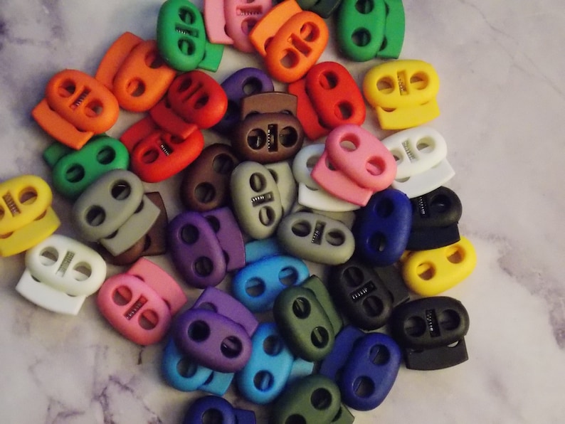 May include: A variety of colorful plastic toggle clasps, also known as cord locks, in various colors including red, blue, green, yellow, purple, gray, brown, and white.