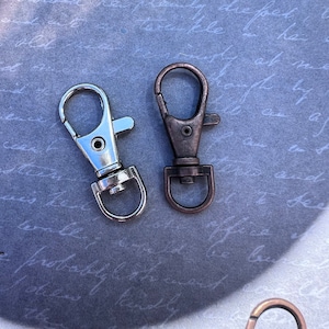 May include: Two metal keychains, one silver and one copper, with a swivel clasp. The keychains are on a gray background.