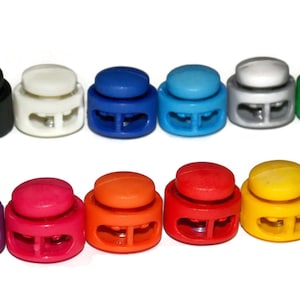 May include: Assortment of 12 plastic toggle clasps in various colors, including black, white, blue, green, purple, red, orange, yellow, and dark green. Each clasp has two holes for attaching cords or straps.