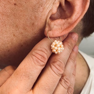 May include: Gold hoop earrings with a cluster of small, cream-coloured pearls.