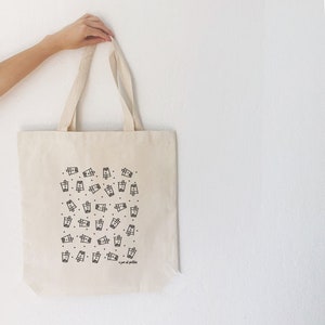 May include: A white canvas tote bag with a black and white illustration of boba tea cups. The text "a cup of bubbles" is printed on the bag.