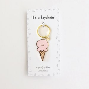 May include: A pink ice cream cone keychain with a happy face. The keychain is attached to a gold metal ring. The card reads "it's a keychain!" and "a jar of pickles".