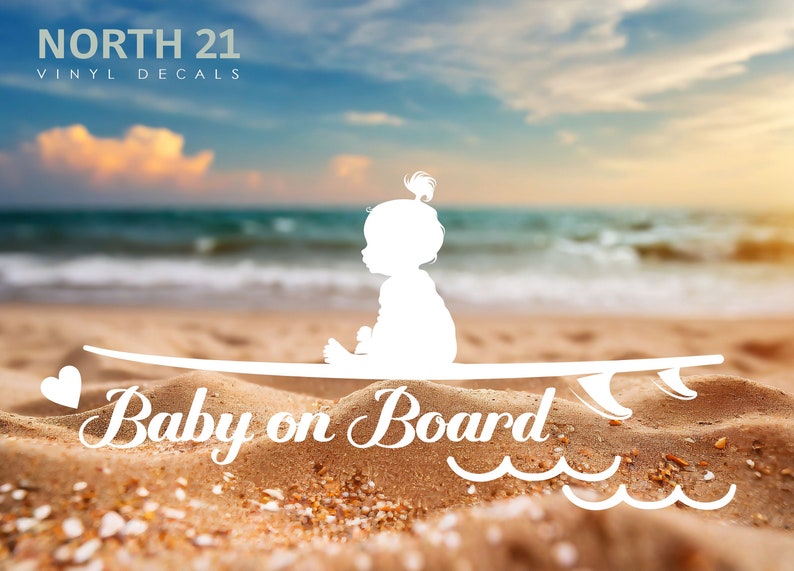 May include: White vinyl decal of a baby sitting on a surfboard with the text "Baby on Board" and wavy lines below. The decal is on a sandy beach with a blue ocean and sky in the background.