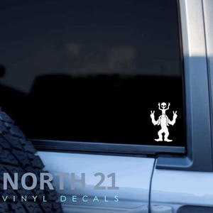 May include: White vinyl decal of a Bigfoot with an alien riding on his shoulders. The decal is on the back window of a car. The text "NORTH 21 VINYL DECALS" is visible on the car.