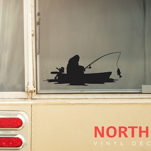 Pode incluir: Adesivo de vinil em silhueta preta e branca de um urso pescando de um barco. O adesivo está sobre um fundo branco e diz "NORTH 21 VINYL DECALS" na parte inferior.