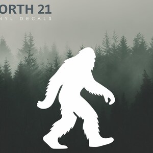 May include: White vinyl decal of a Bigfoot silhouette walking to the right. The decal is set against a backdrop of a misty forest with evergreen trees. The text "NORTH 21 VINYL DECALS" is at the top left.
