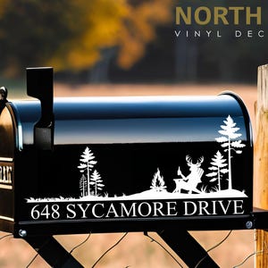 May include: Black mailbox with a white decal featuring a deer relaxing by a campfire, trees, and the text "648 SYCAMORE DRIVE." The mailbox also has the text "NORTH 21 VINYL DECALS."