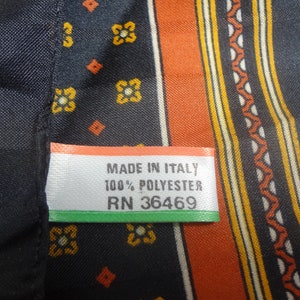 Op de afbeelding: Een zwarte en oranje stof met een wit label waarop staat "Made in Italy 100% Polyester RN 36469".