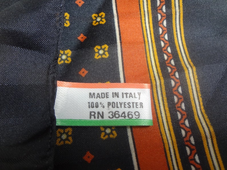 Op de afbeelding: Een zwarte en oranje stof met een wit label waarop staat "Made in Italy 100% Polyester RN 36469".