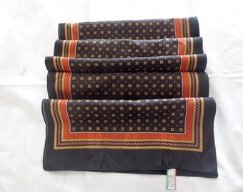 May include: A black silk scarf with a repeating pattern of small orange and gold squares. The scarf has a red and gold border.