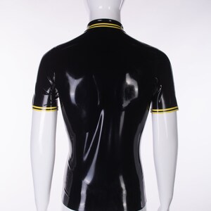 May include: Black short-sleeved shirt with yellow trim around the collar and sleeves. The shirt is made of shiny latex.