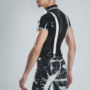 May include: A person wearing a black latex shirt with white trim and white suspenders. The person is also wearing black latex pants with a white splatter paint design. The text "coco-latex" is visible in the top left corner of the image.