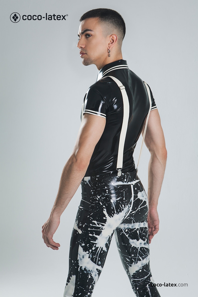 May include: A person wearing a black latex shirt with white trim and white suspenders. The person is also wearing black latex pants with a white splatter paint design. The text "coco-latex" is visible in the top left corner of the image.