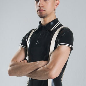 May include: A black latex polo shirt with white trim and suspenders. The shirt has a collar and short sleeves. The model is wearing black and white latex pants with a splatter pattern.