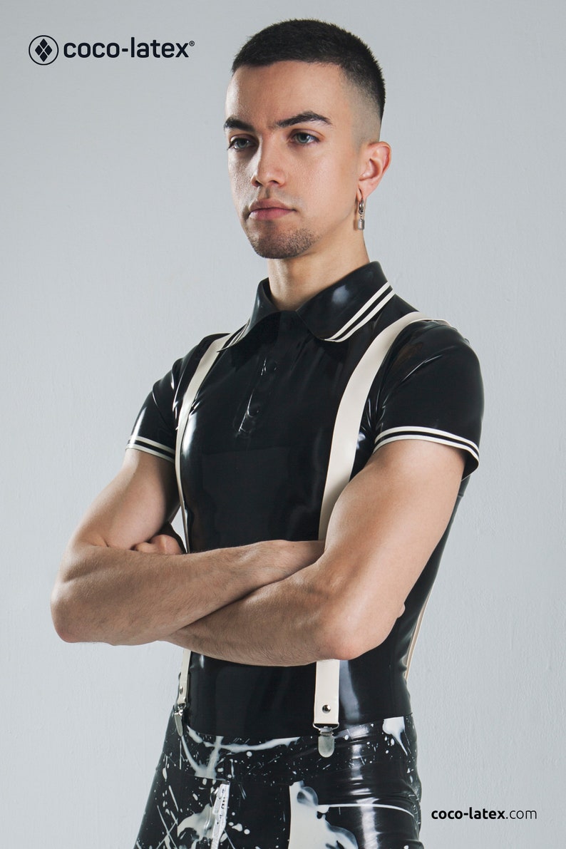 May include: A black latex polo shirt with white trim and suspenders. The shirt has a collar and short sleeves. The model is wearing black and white latex pants with a splatter pattern.