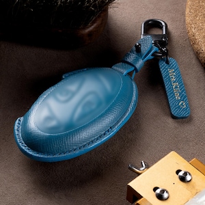 A blue leather car keychain with a keyring attached, resting on a surface with other items.